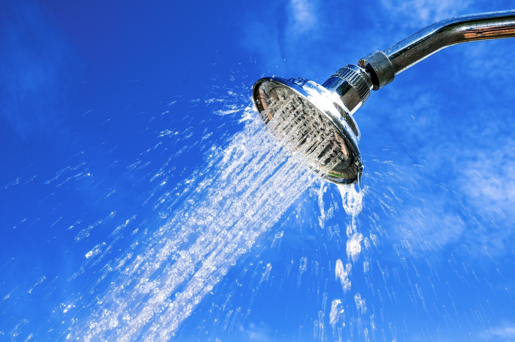 Close-up of outdoor shower head with water flow against blue sky.